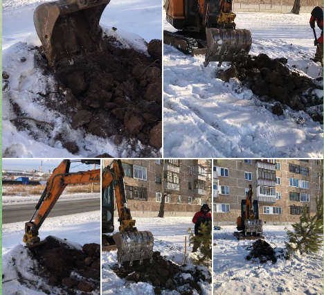 Экскаватор копает землю зимой возле дома.