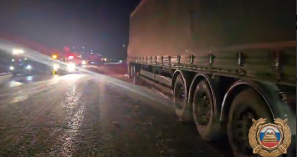 Большой грузовик на ночной дороге со включёнными фарами.