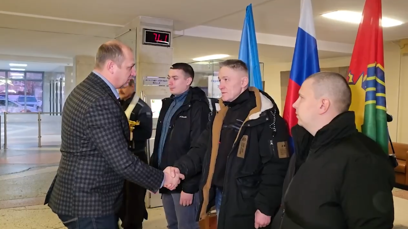 Мужчина пожимает руку трем людям возле флагов.