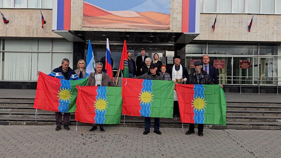 Люди держат цветные флаги перед зданием.