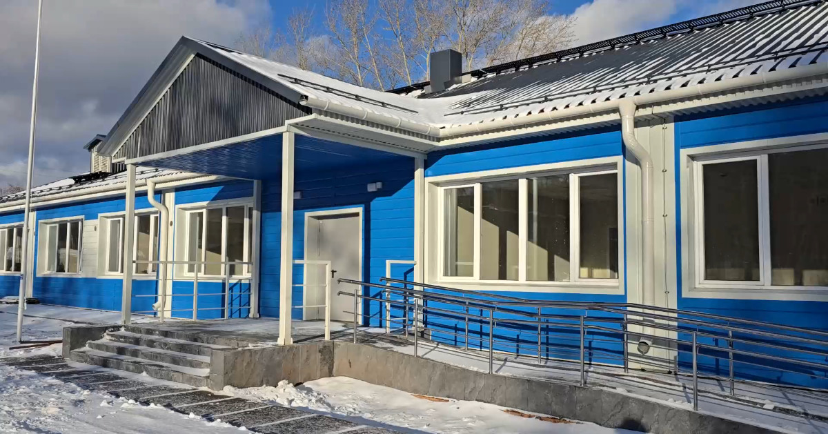 Синее здание зимой с пандусами и ступенями.