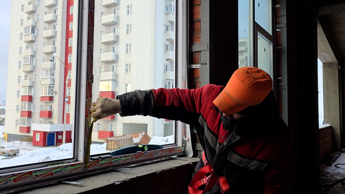 Рабочий измеряет оконную раму в квартире.