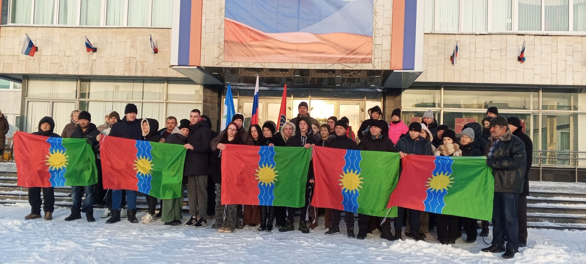 Люди с флагами стоят перед зданием на снегу.