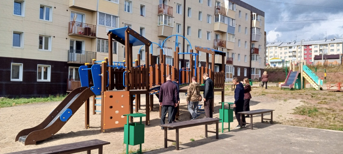 Детская площадка возле многоквартирного дома, люди гуляют.