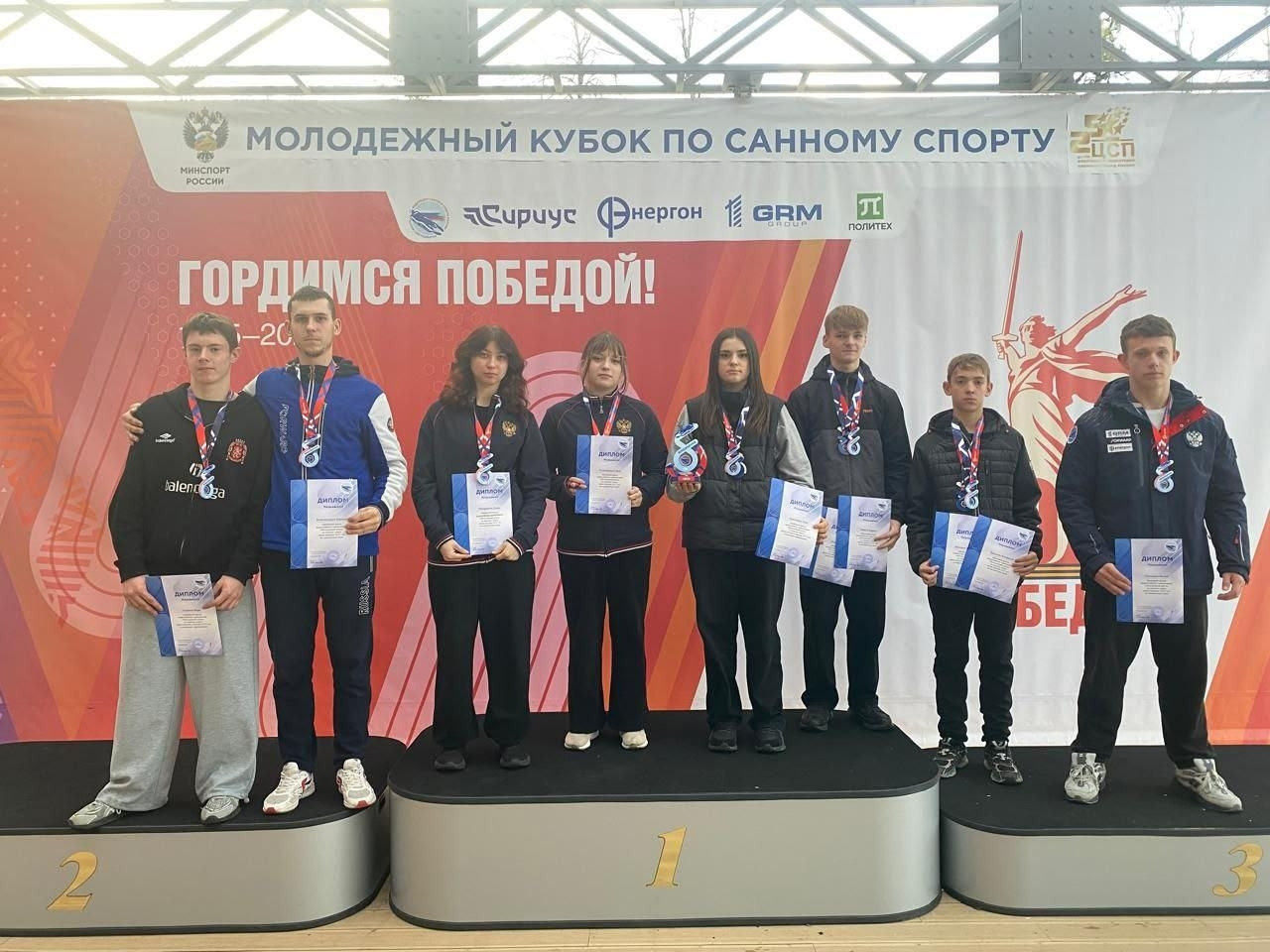 Молодежные победители санного спорта с медалями и дипломами.