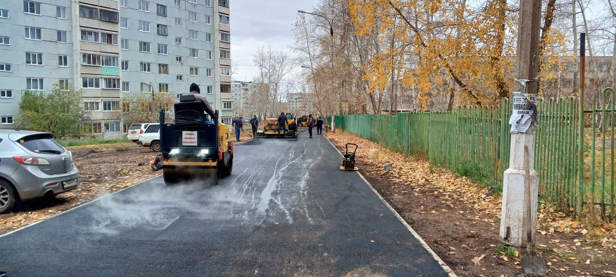 Рабочие укладывают асфальт во дворе жилого дома.