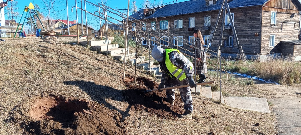 Работник копает яму около деревянного дома.