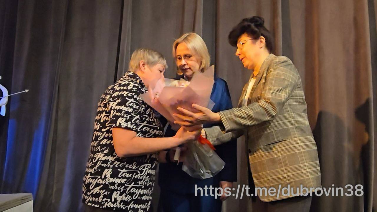 Три женщины обмениваются цветами на сцене.