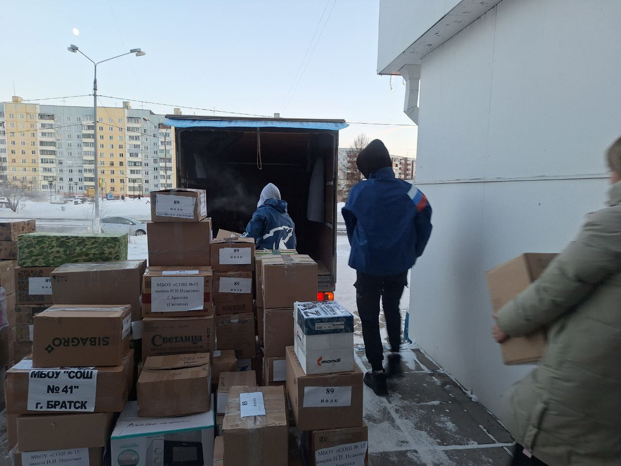 Грузчики разгружают коробки на фоне жилых домов.