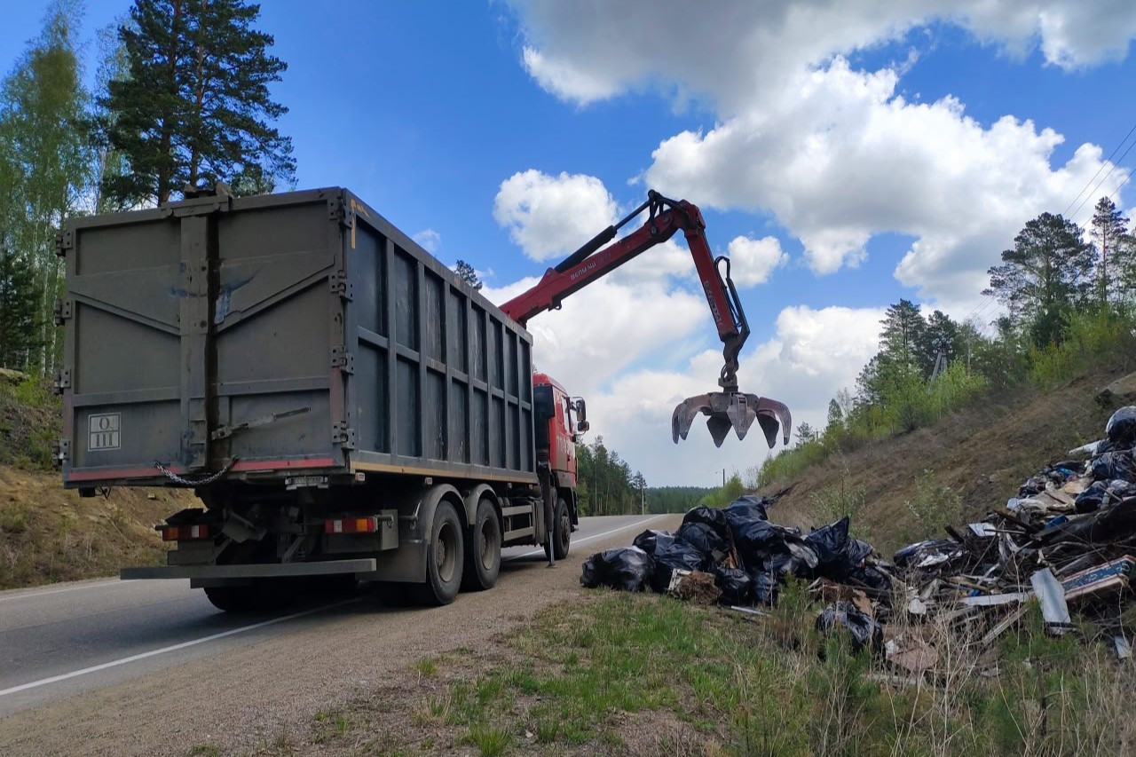 Грузовик убирает мусор вдоль лесной дороги.