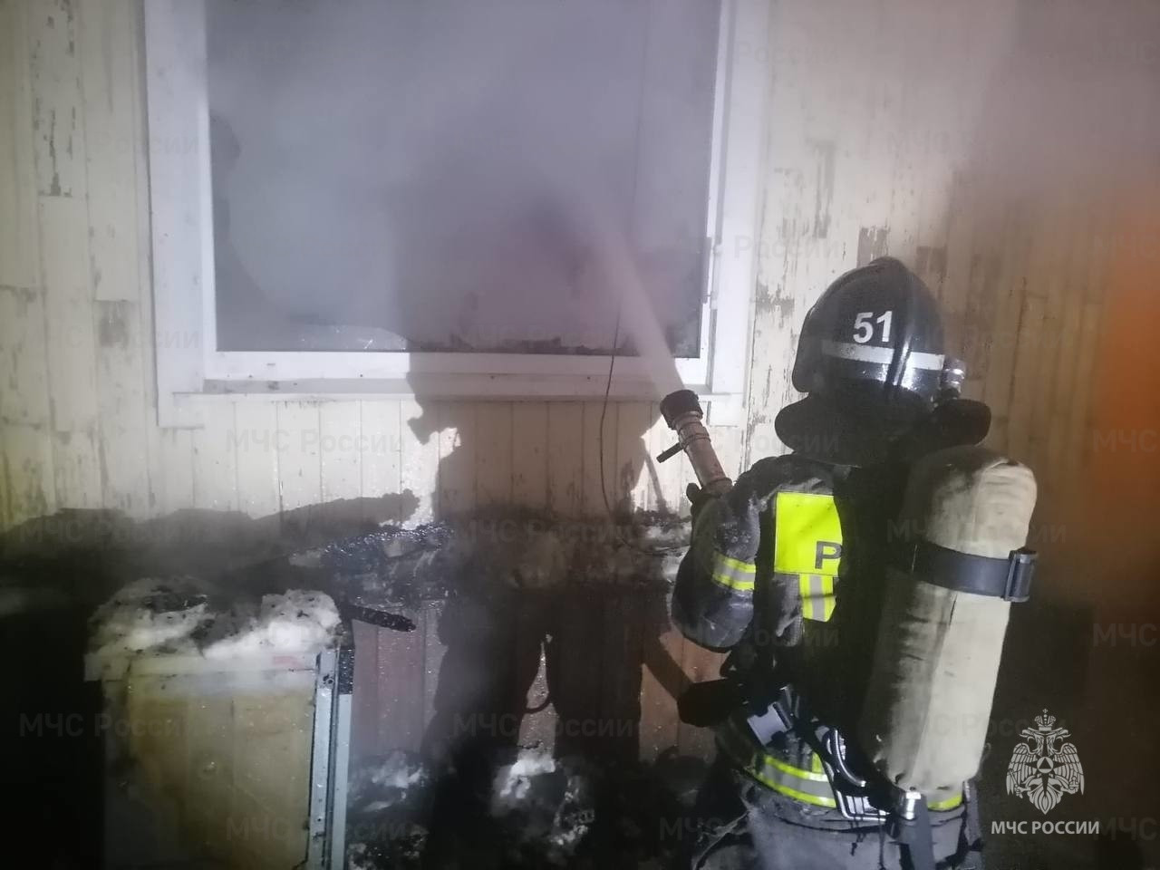 Пожарный тушит огонь в здании ночью.