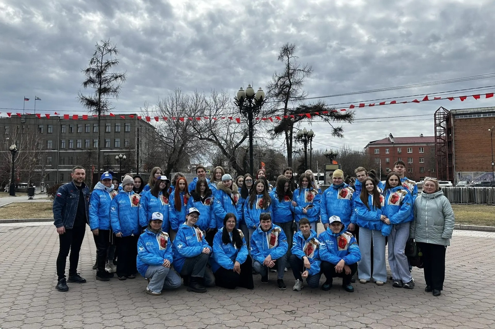 Группа молодых людей в синих куртках на площади