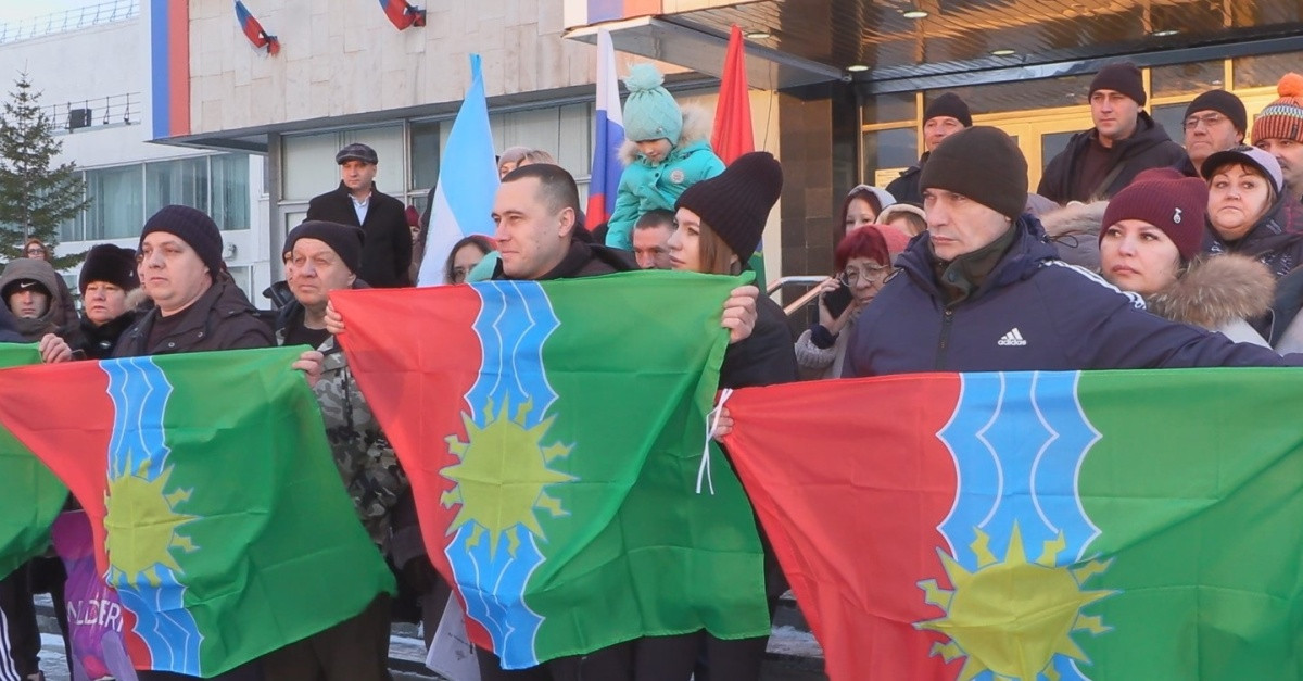 Группа людей держит красно-зелёные флаги на митинге.