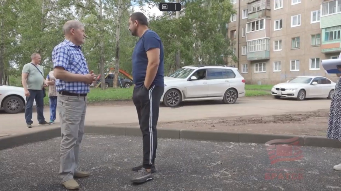 Два человека беседуют на улице перед домом.