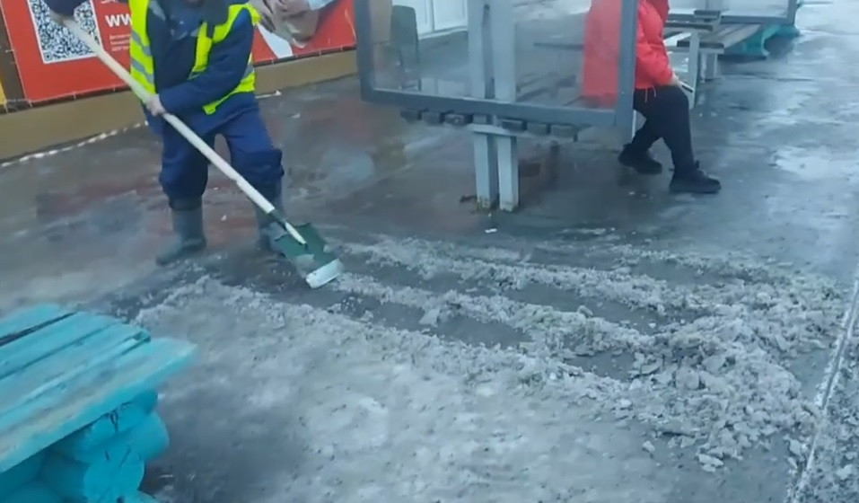 Рабочий убирает снег на остановке.