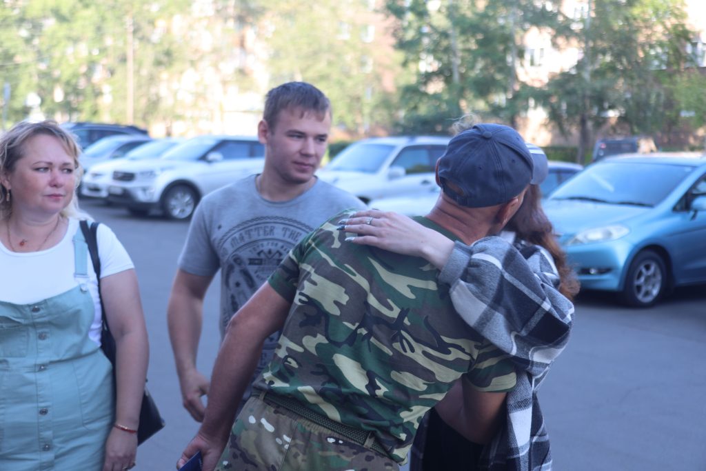 Люди обнимаются на фоне автомобилей.