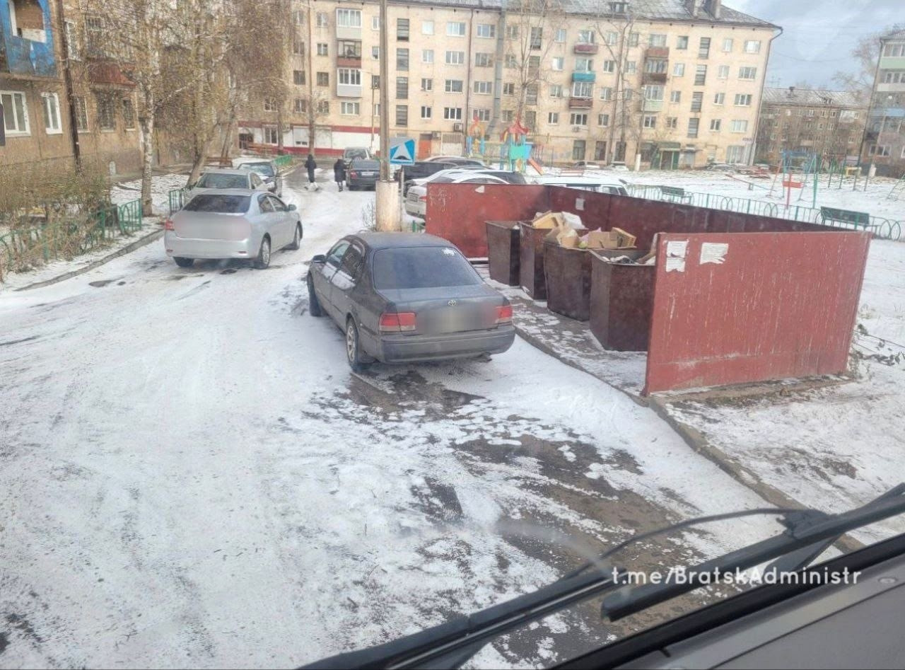 Машины припаркованы возле мусорных баков зимой.