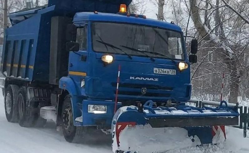 Синий грузовик очищает снег на дороге зимой.