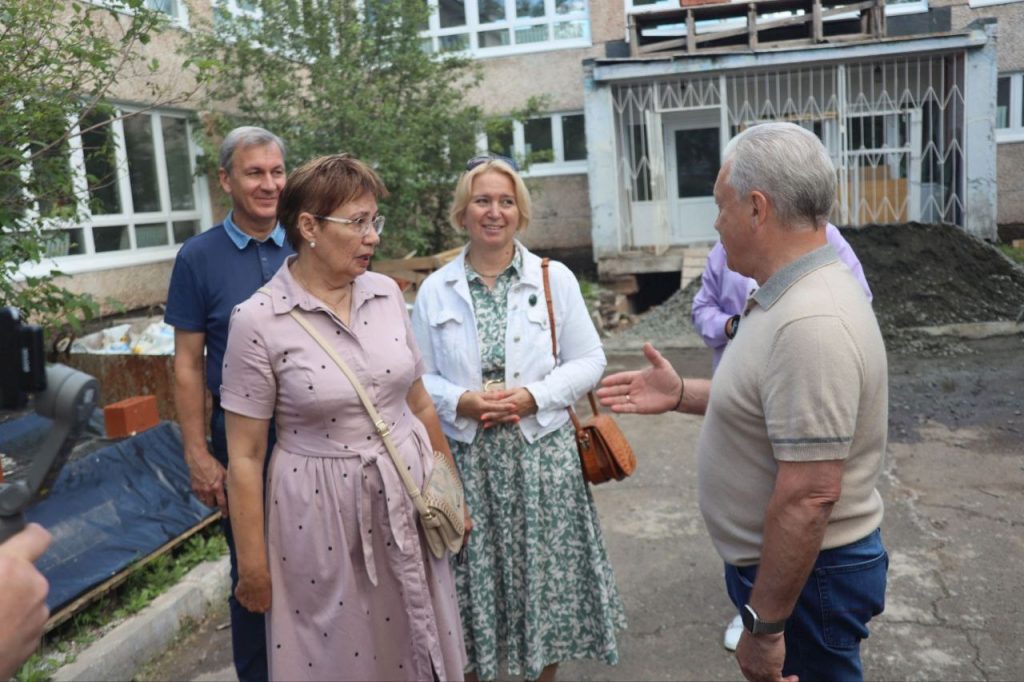 Группа людей обсуждают проект у здания.