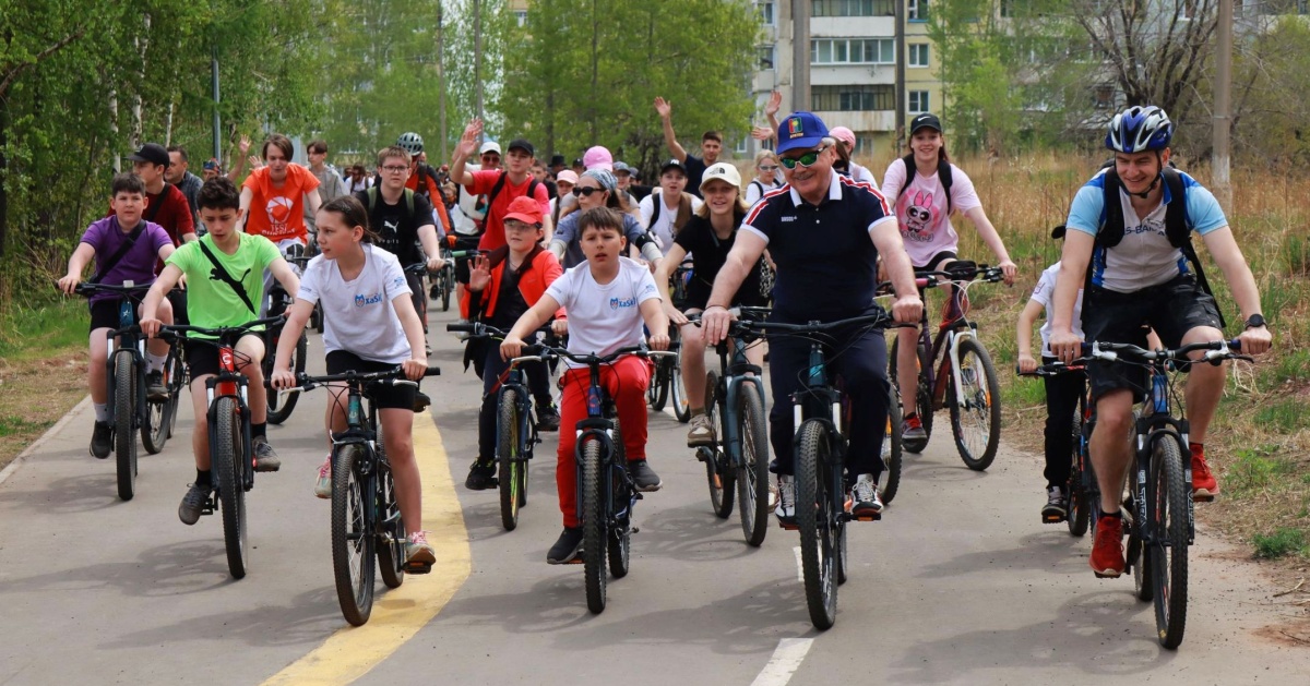 Группа велосипедистов едет по парку в Братске, наслаждаясь совместной велопрогулкой в ясную погоду.