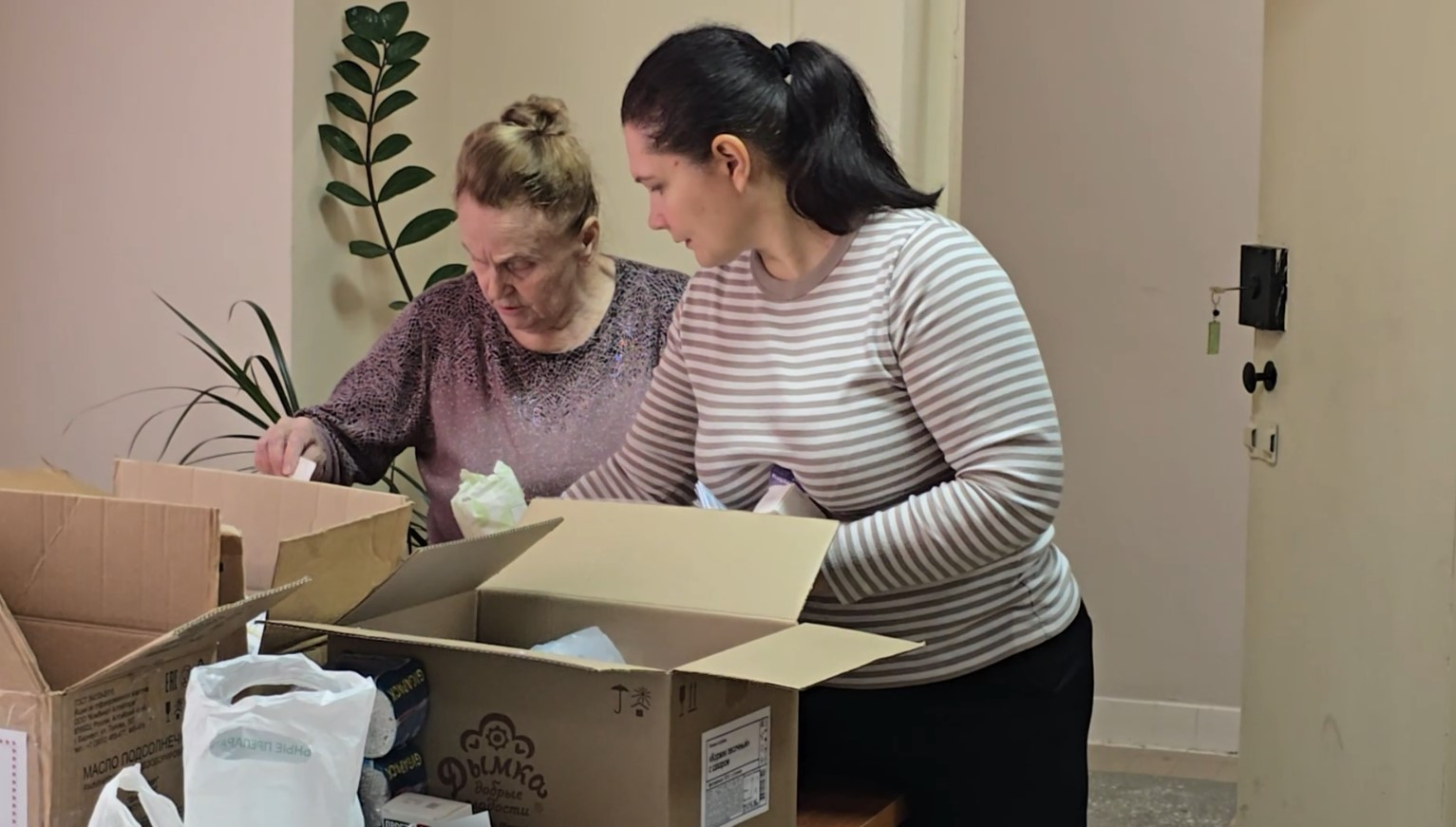 Две женщины сортируют вещи в коробках.