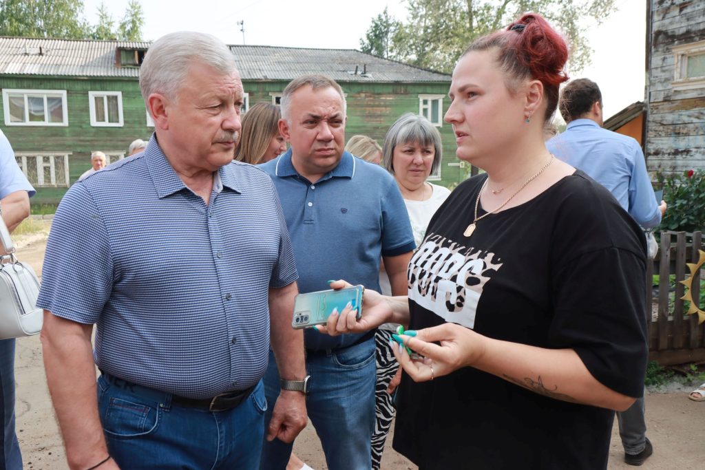 Группа людей разговаривает на улице возле деревянных домов.