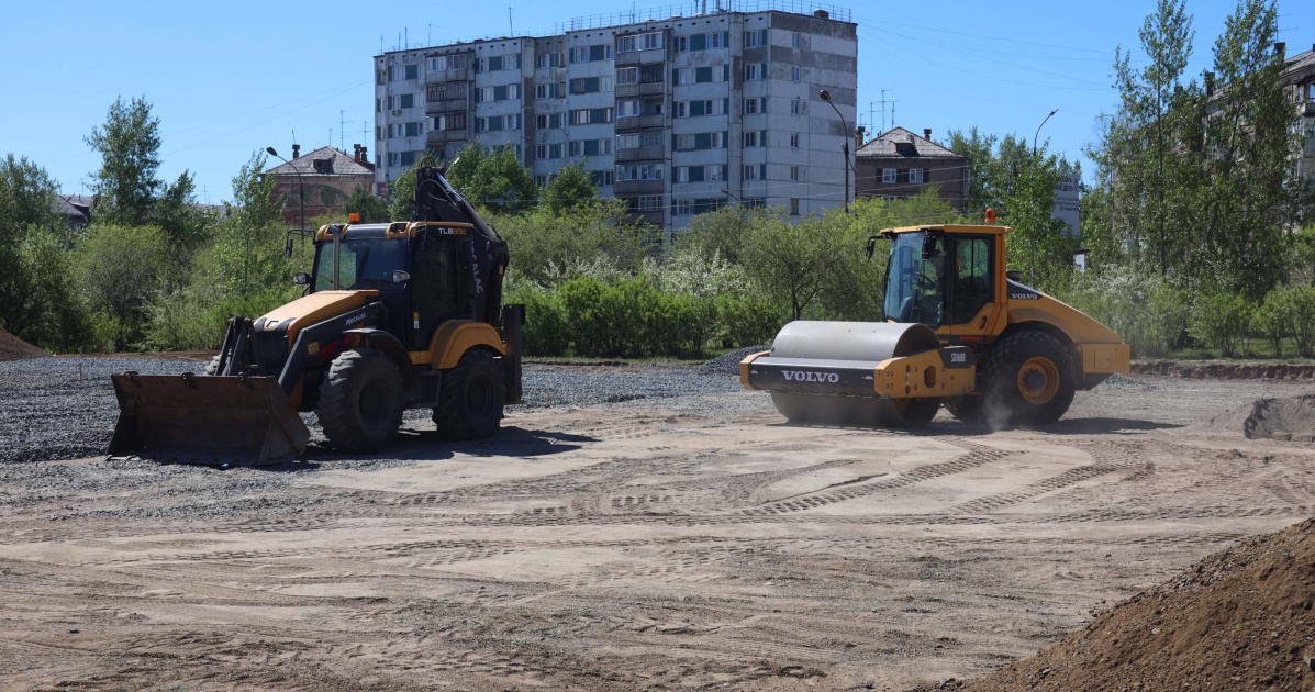 Фронтальный погрузчик и дорожный каток на строительной площадке, ясно и солнечно.