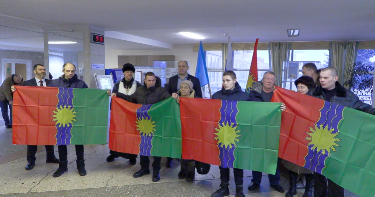 Группа людей держит пестрые флаги в помещении.