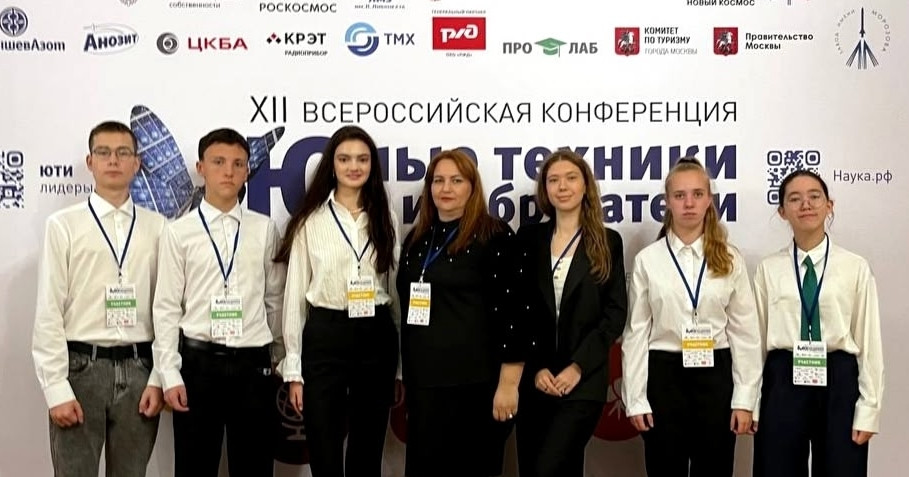 Участники конференции стоят на фоне баннера.