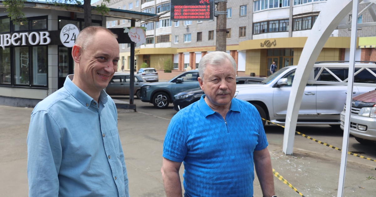 Двое мужчин разговаривают на улице в городе с кириллическими вывесками.