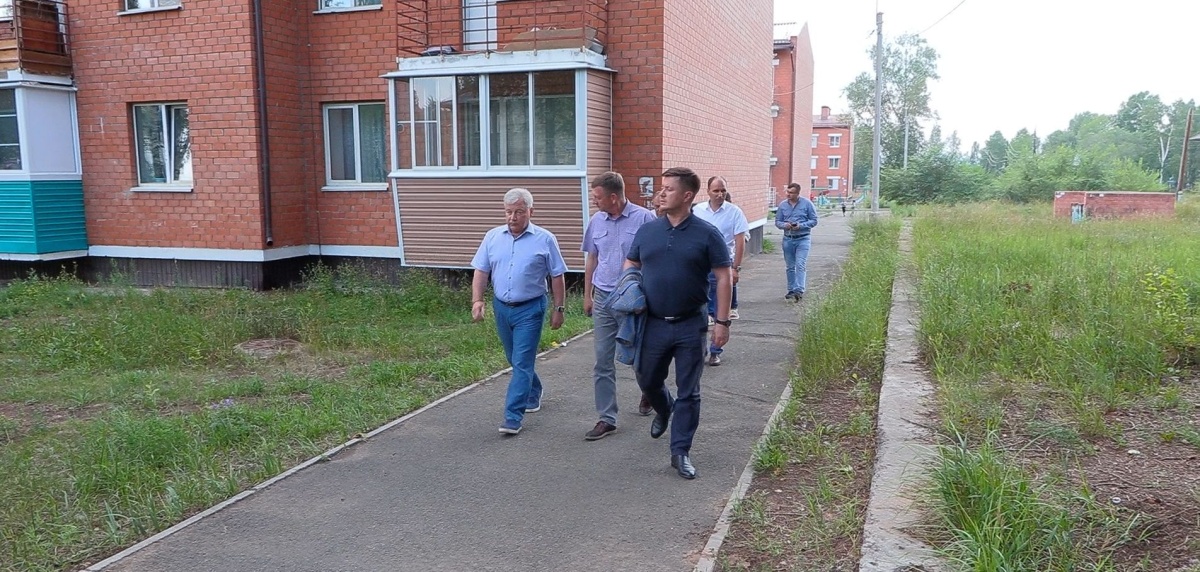 Группа людей идет вдоль кирпичного дома