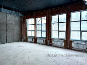 Пустая комната с большими окнами и радиаторами.