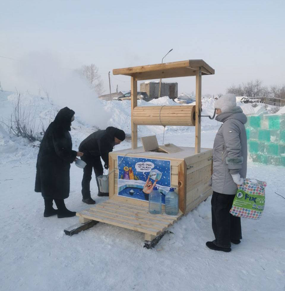 Люди набирают воду из деревянного колодца на снегу.