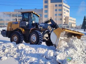 Погрузчик убирает снег возле здания.