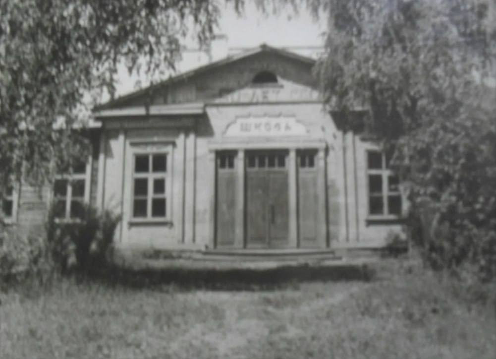 Старое здание школы с деревьями перед входом.