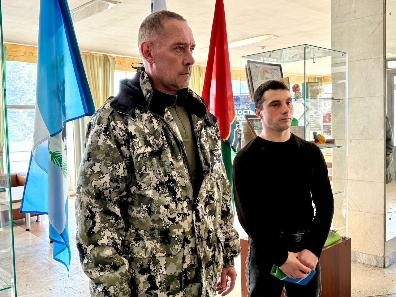 Два человека возле флагов в помещении