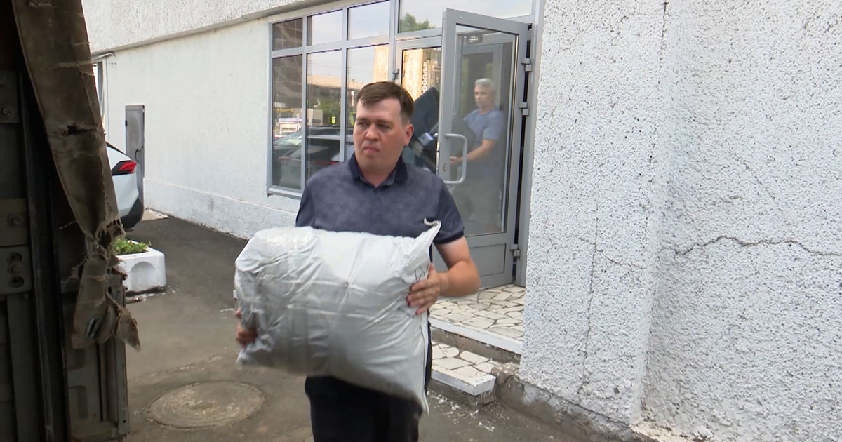 Мужчина несет мешок у здания.