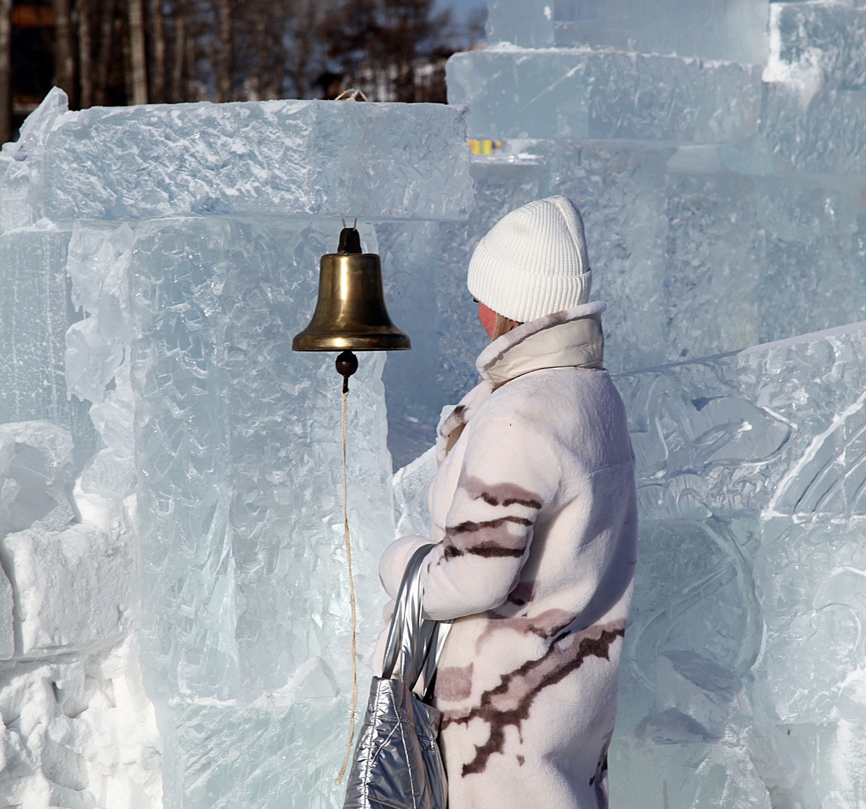 Человек звонит в колокол среди льдин зимой.