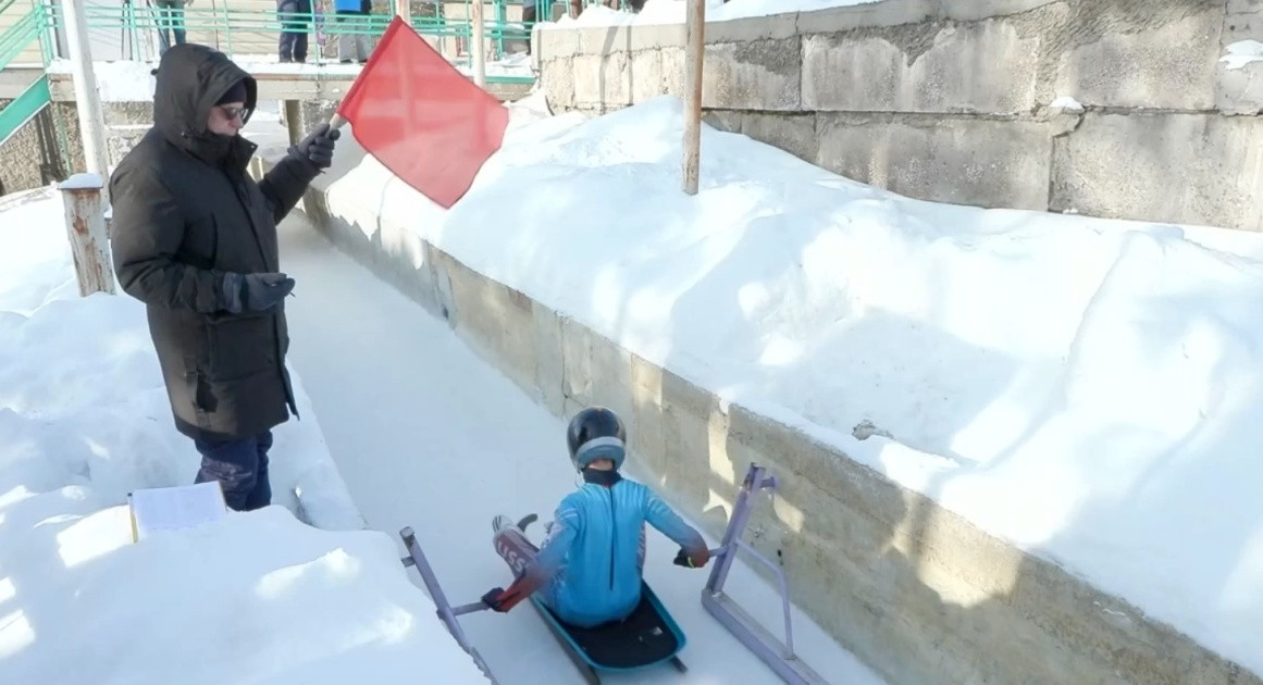 Человек со снежной трассой и спортсменом на санях.