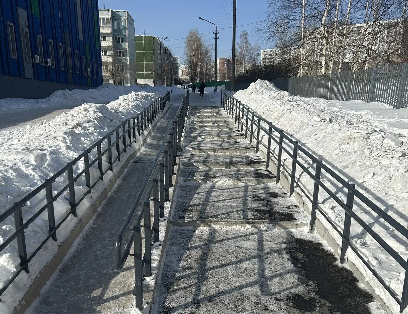 Зимняя улица с заснеженной дорогой и перилами.