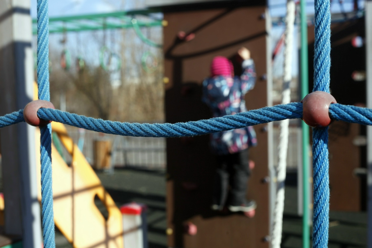 Ребёнок на игровой площадке с сеткой и стенкой.