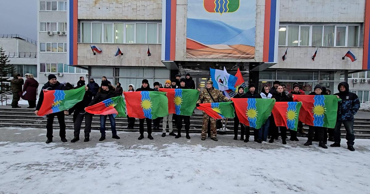 Группа людей с флагами на фоне здания.