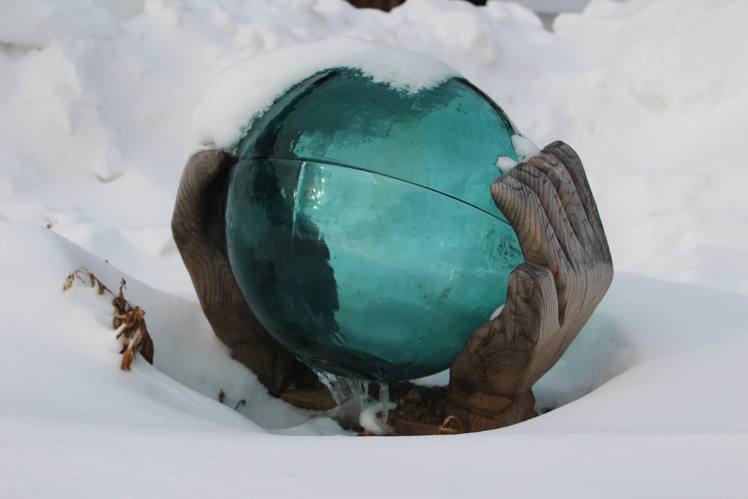 Деревянные руки держат стеклянный шар в снегу.