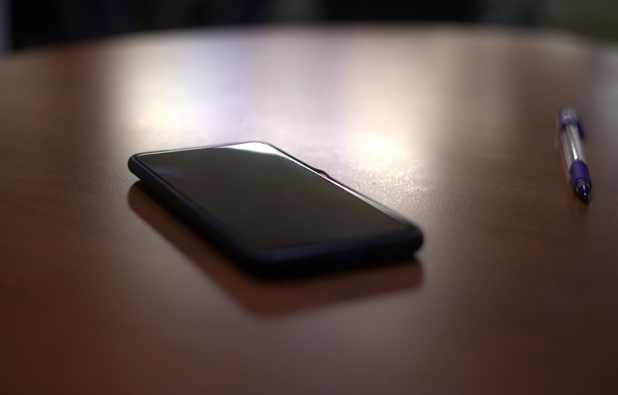 Смартфон и ручка лежат на деревянном столе.