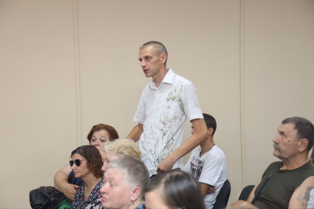 Мужчина встает среди сидящих людей.