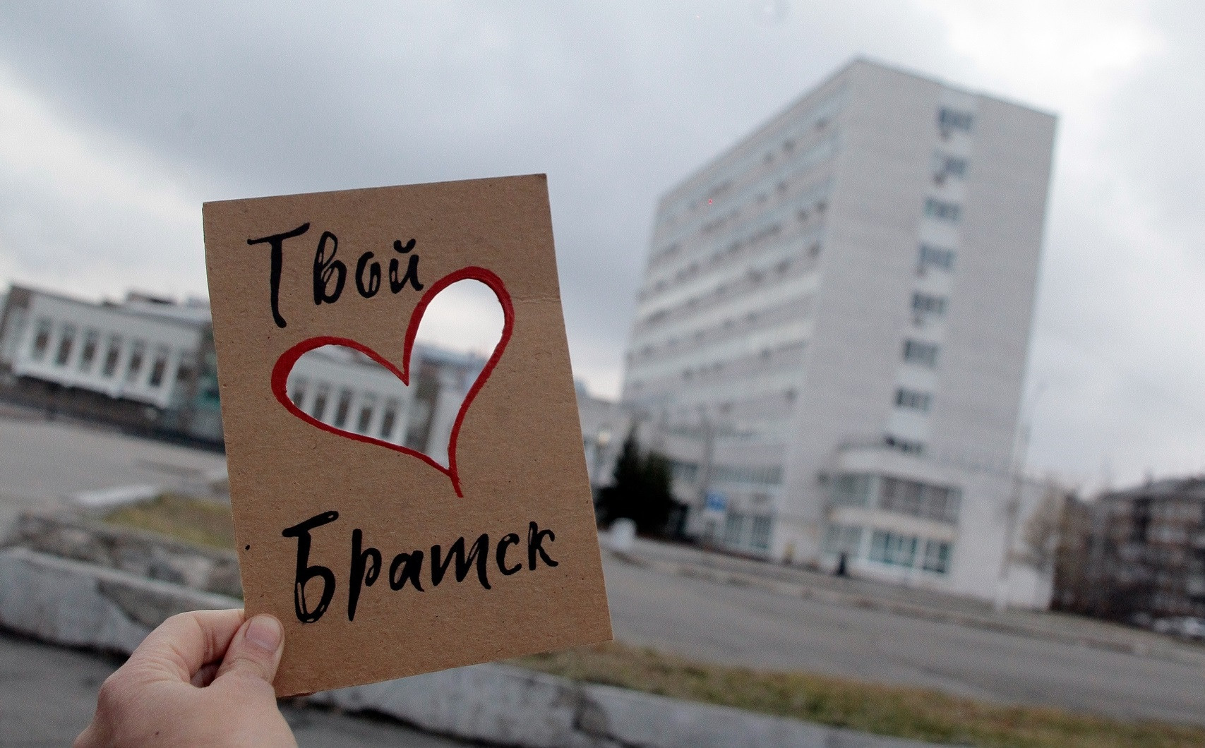 Человек держит картонку с надписью перед зданием.