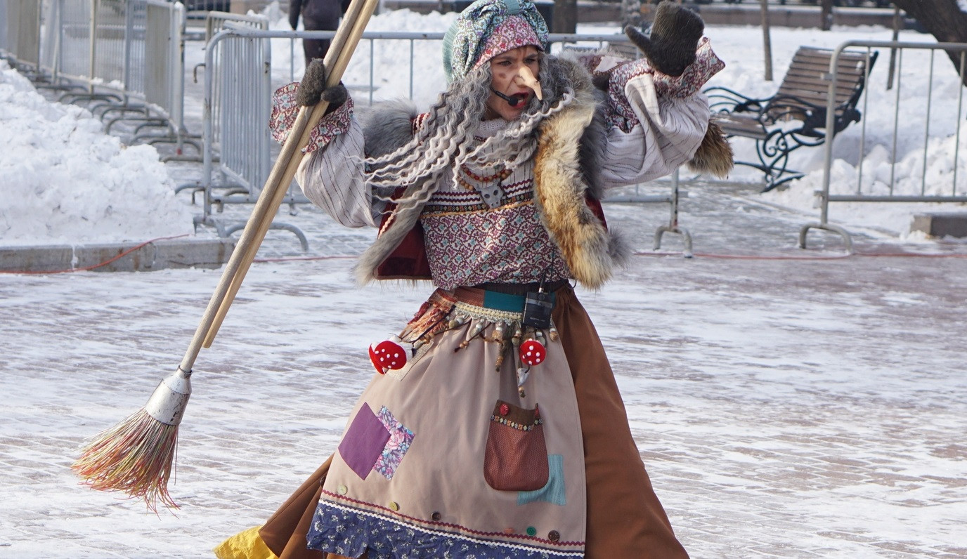 Человек в костюме Бабы Яги с метлой на улице.