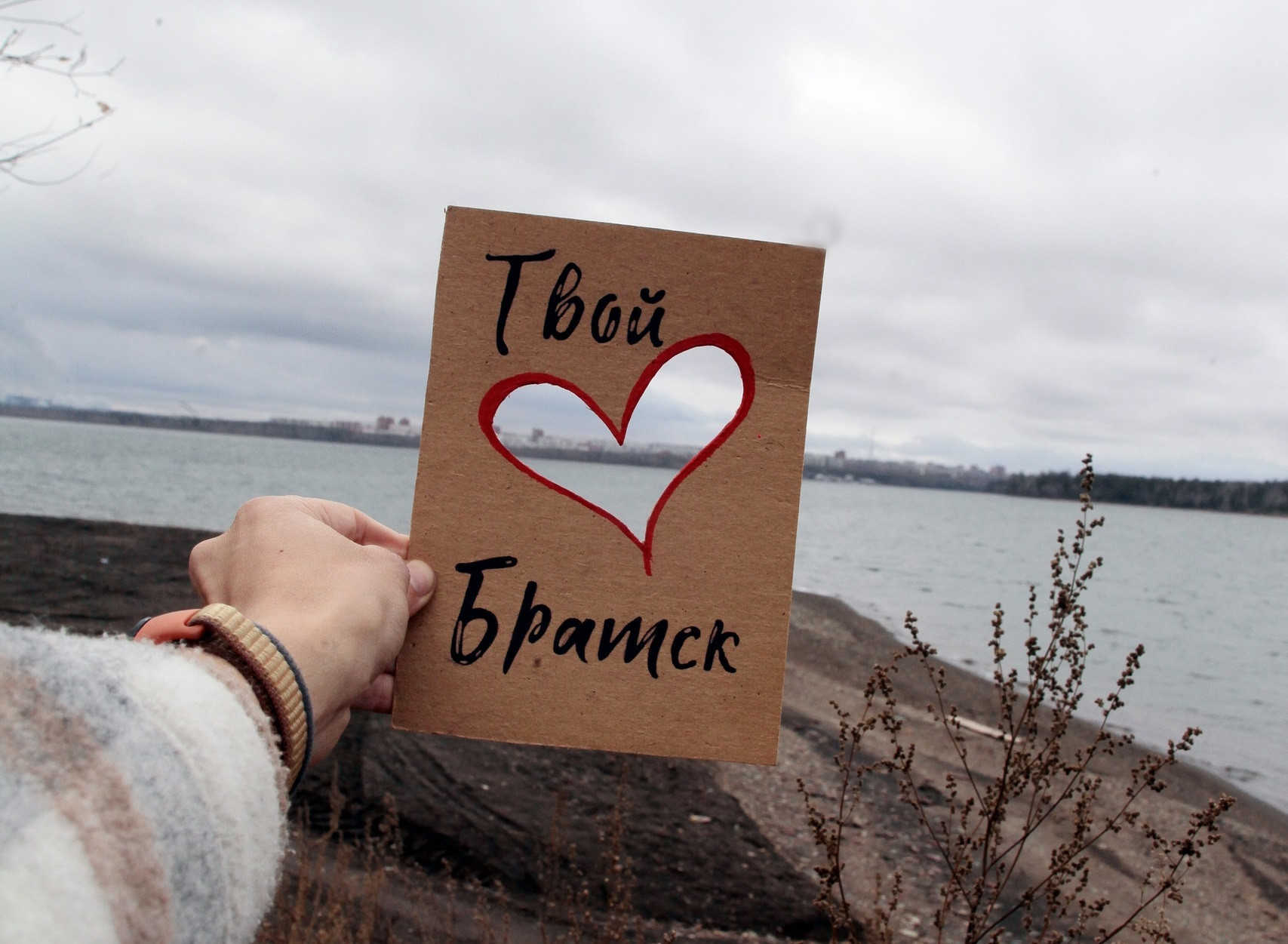 Рука держит табличку с текстом у реки